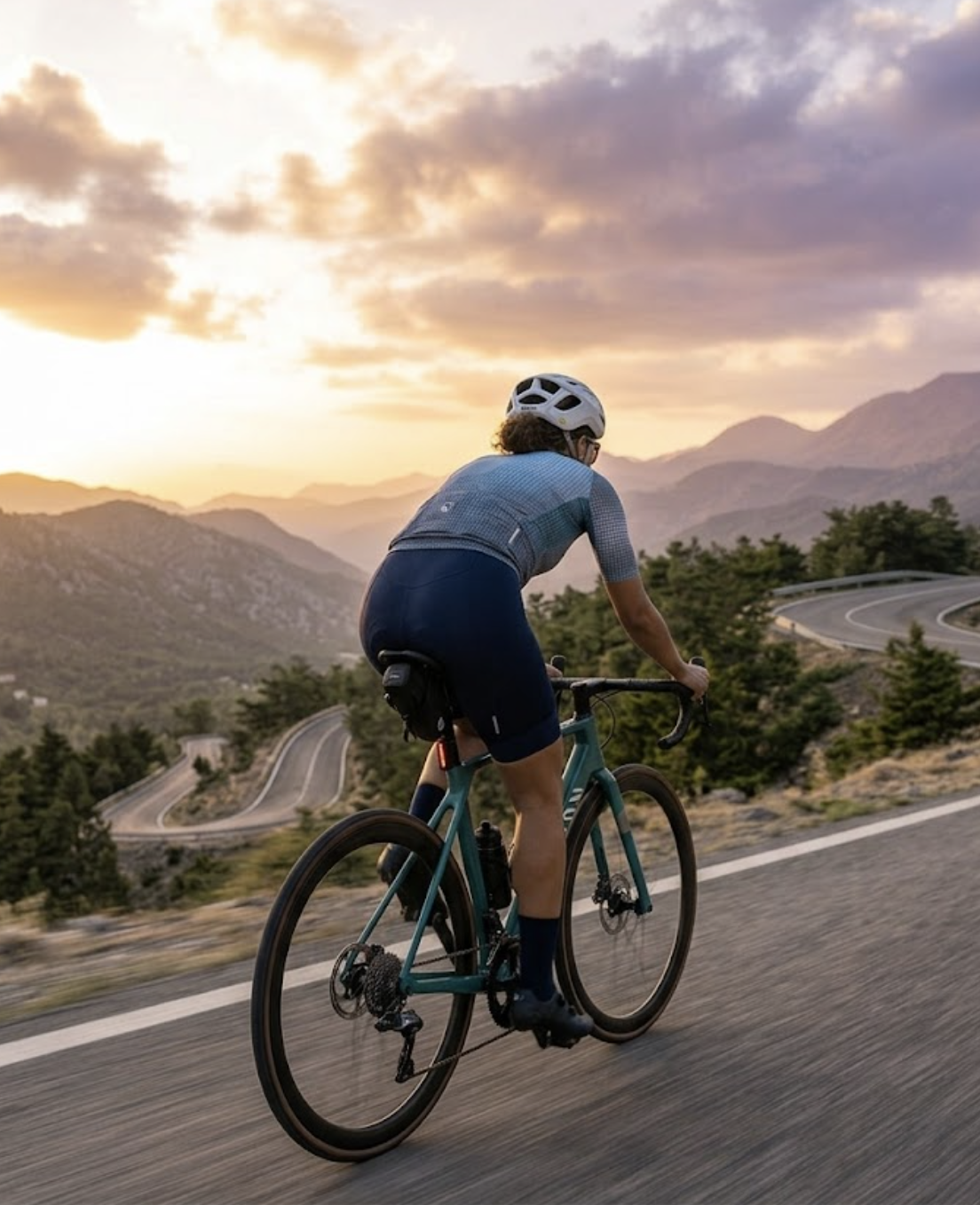 A cyclist riding toward a mountain sunset on a winding road